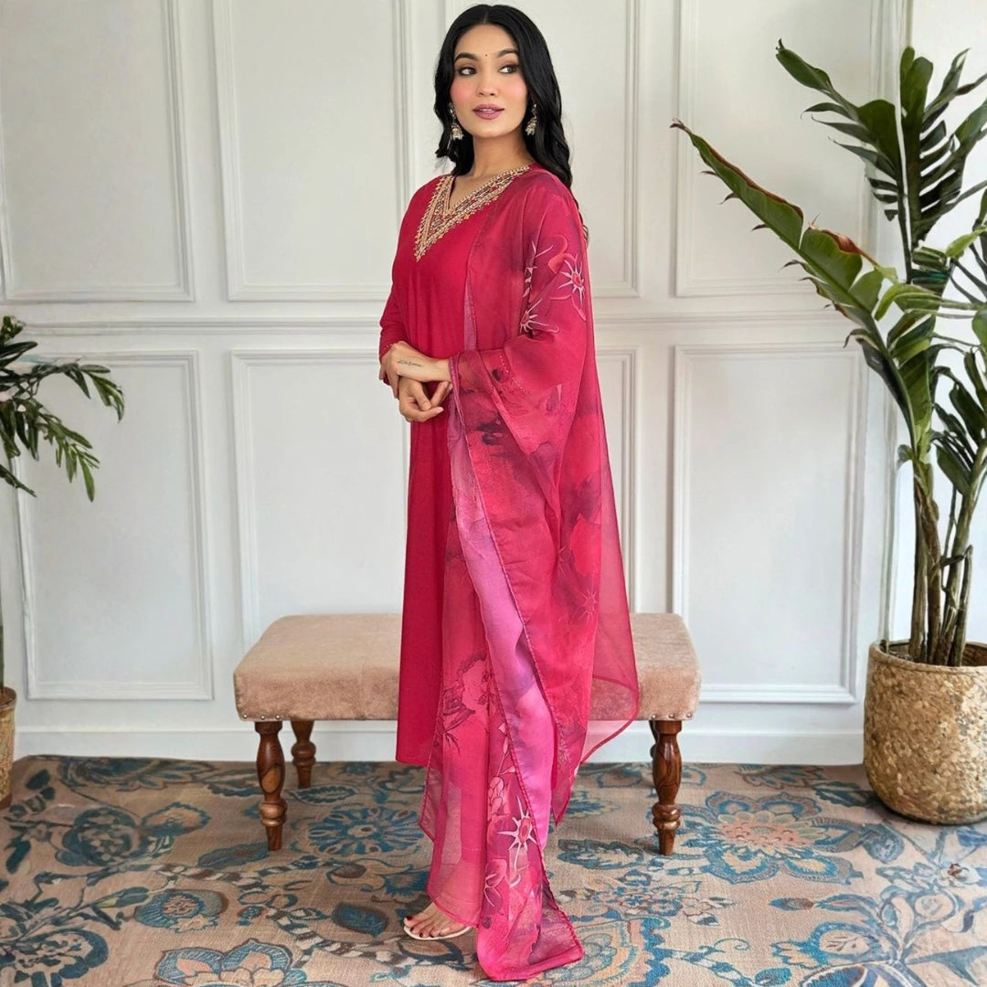 Woman in a red saree standing in a room with plants and a patterned rug.